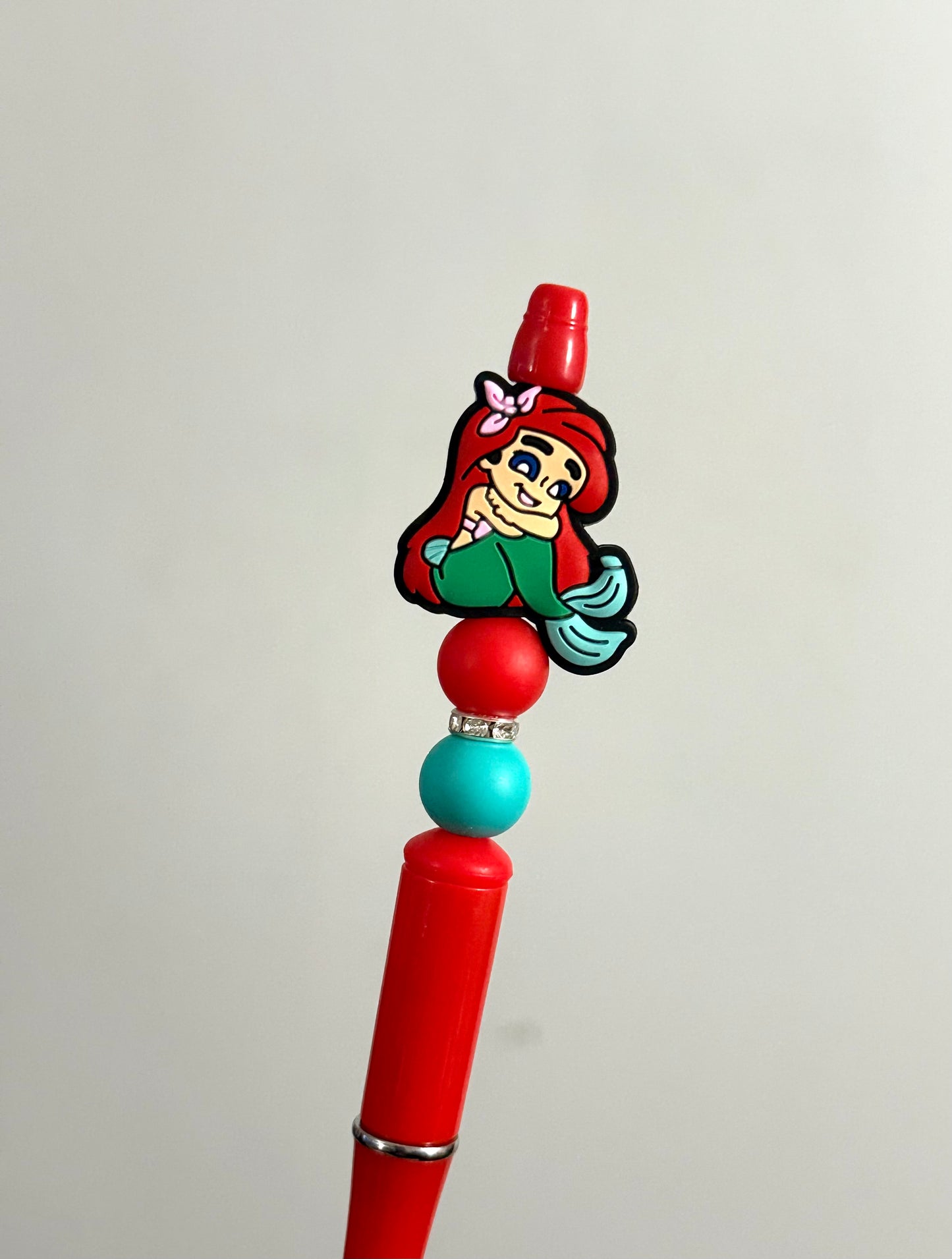 Handmade red beaded pen inspired by little mermaid, featuring red and teal beads and an Alice character charm